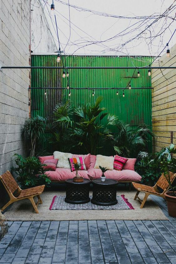 A-bright-tropical-patio-with-a-pink-sofa-and-printed-pillows-leather-chairs-lots-of-lush-plants-in-pots-and-black-tables