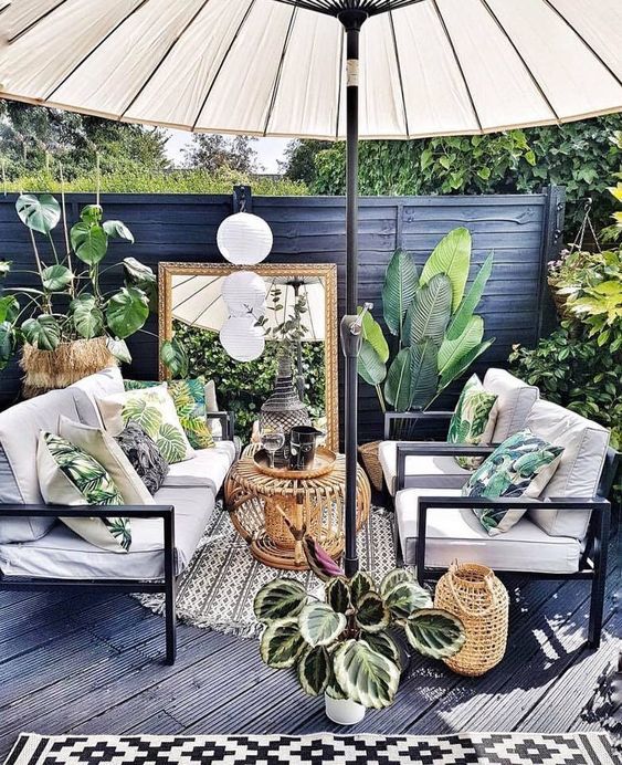 A-small-tropical-patio-done-in-black-and-grey-with-white-furniture-a-large-umbrella-potted-plants-and-tropical-pillows
