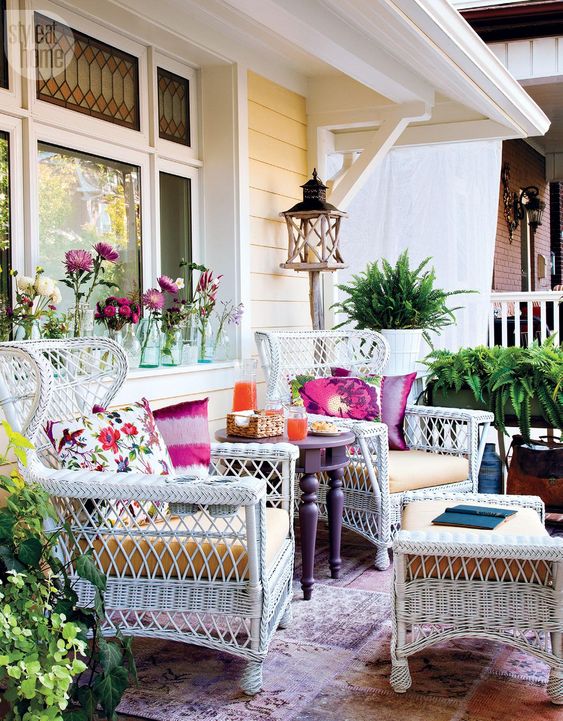 A-colorful-summer-porhc-with-white-wicker-furniture-a-purple-table-lots-of-greenery-printed-pillows-and-potted-greenery