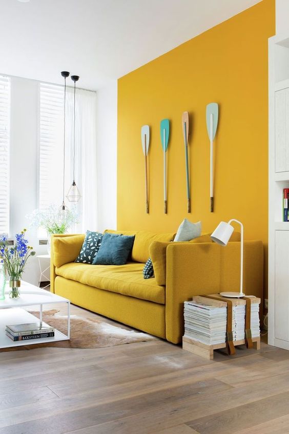 A-bright-modern-living-room-with-a-mustard-accent-wall-and-a-matching-sofa-pendant-lamps-and-oars-on-the-wall