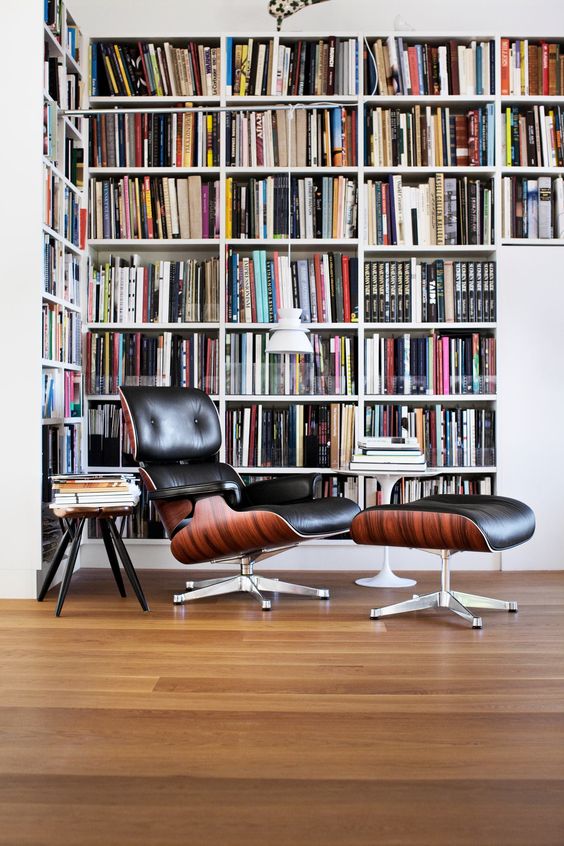 A-modern-home-library-nook-with-an-oversized-l-shaped-bookcase-a-black-leather-chair-with-a-footrest