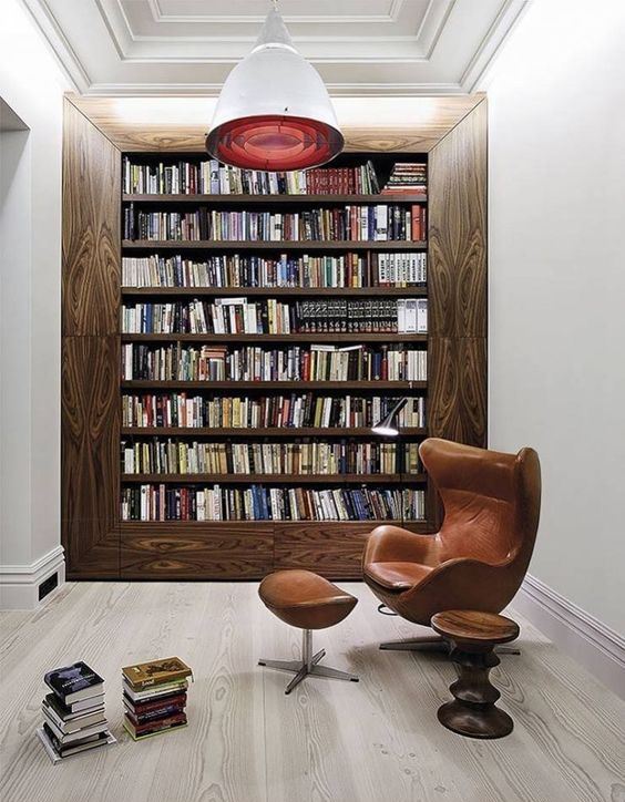 A-modern-home-library-with-a-bookcase-in-a-wide-wooden-frame-with-a-comfy-leather-chair-and-a-red-pendant-lamp