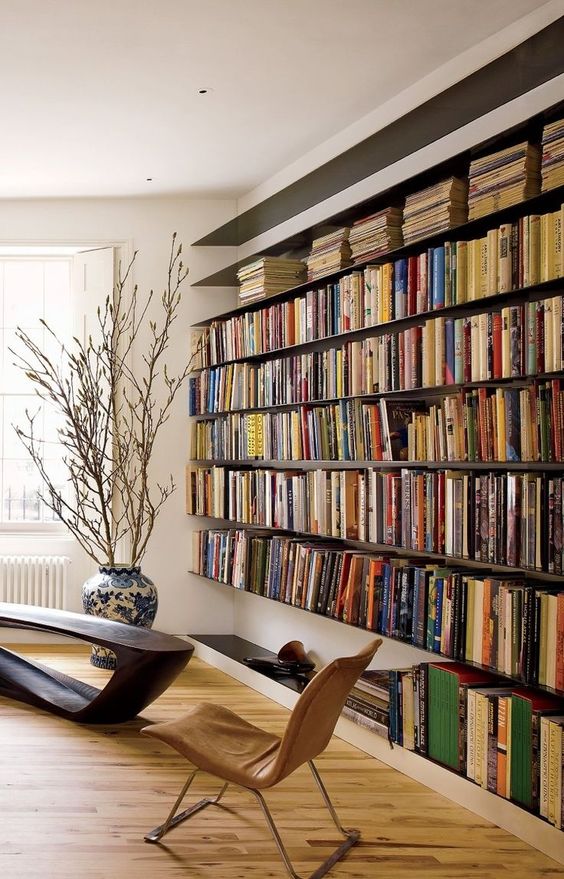A-modern-refined-home-library-with-an-oversized-floating-bookshelf-unit-a-dark-wooden-table-and-a-leather-chair