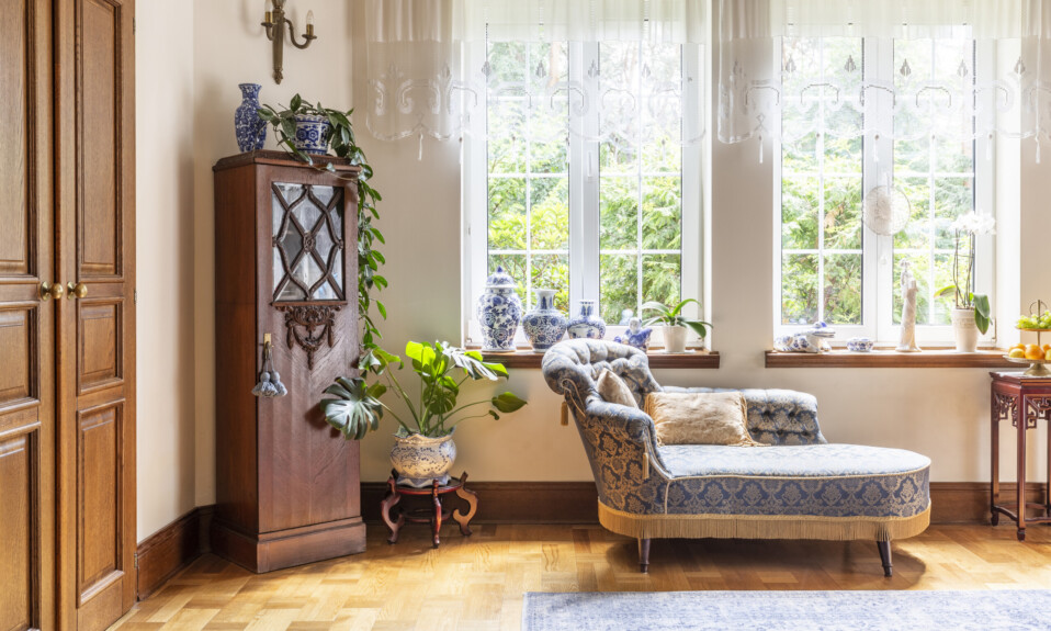 A luxurious living room interior with a couch and a wooden cabinet standing on a parquet against two large windows. real photo.