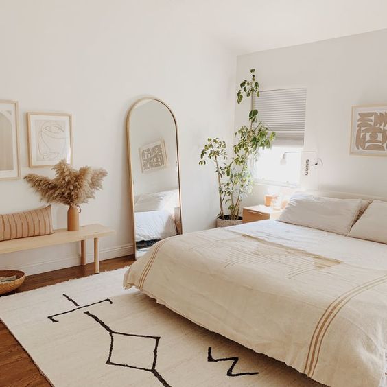 1-a-neutral-boho-bedroom-with-a-bed-a-wooden-bench-a-curved-mirror-potted-plants-and-artworks