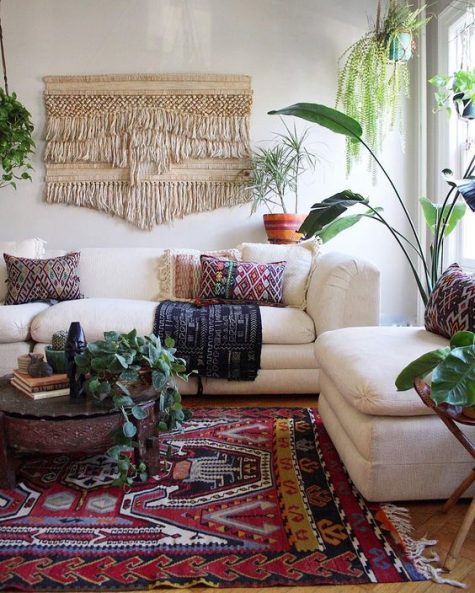 A-colorful-boho-living-space-with-a-macrame-hanging-a-boho-rug-and-pillows-potted-greenery-and-neutral-furniture