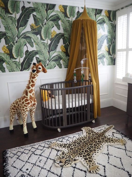 A-jungle-nursery-with-a-tropical-leaf-wall-a-dark-crib-a-mustard-canopy-a-fun-rug-and-a-toy-giraffe