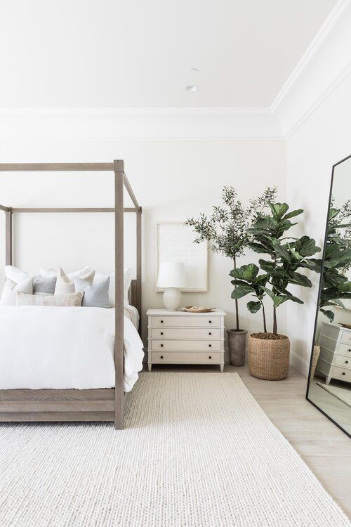 A-neutral-modern-bedroom-with-a-wooden-bed-statement-plants-an-oversized-mirror-and-white-nightstands