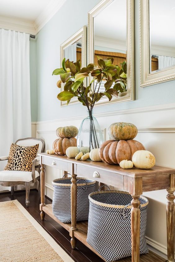 09-a-vintage-farmhouse-console-table-with-chevron-baskets-natural-pumpkins-stacked-on-each-other-and-fall-leaves-in-a-vase