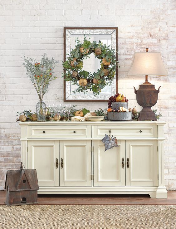 21-a-harvest-themed-console-table-with-faux-pumpkins-greenery-pinecones-faux-fruit-on-a-metal-stand