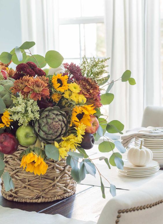 A-bold-fall-centerpiece-of-yellow-orange-and-rust-and-burgundy-blooms-greenery-faux-apples-and-pears-plus-foliage
