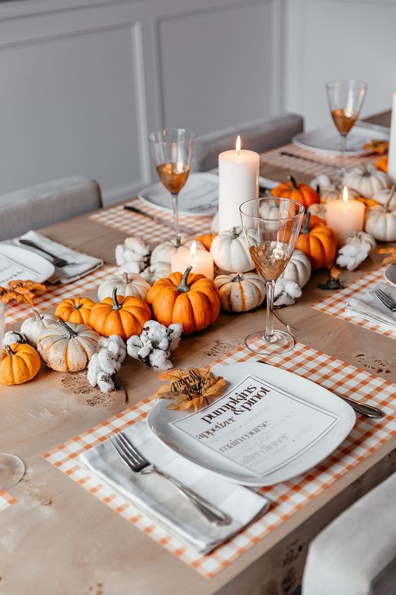 A-bright-fall-tablescape-with-plaid-placemats-a-bold-fall-centerpiece-of-neutral-and-orange-pumpkins-plus-candles