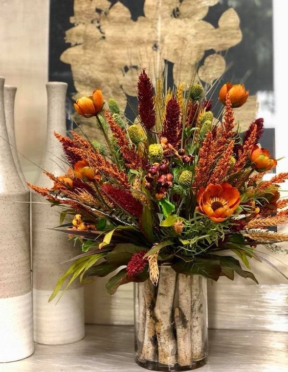 A-bright-rustic-arrangement-of-rust-burgundy-faux-blooms-dried-herbs-and-greenery-and-wooden-sticks-in-the-vase
