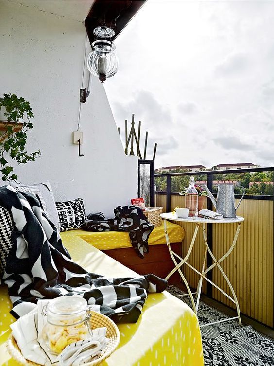 A-bright-summer-balcony-with-a-corner-bench-and-yellow-black-and-white-textiles-a-shabby-chic-table-and-a-potted-plant