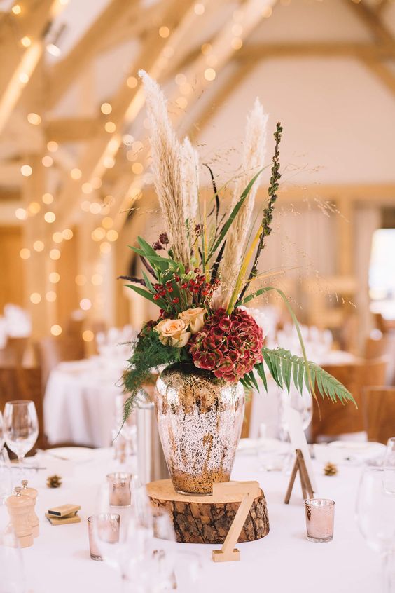 A-chic-wedding-centerpiece-of-a-mercury-glass-vase-and-rust-and-red-blooms-pampas-grass-and-ferns