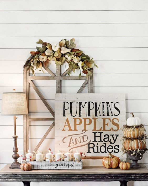 A-chic-whitewashed-wooden-sign-with-black-and-rust-colored-letters-pumpkins-and-candles-around