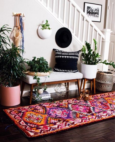 A-colorful-entryway-with-a-white-bench-a-colorful-boho-rug-potted-plants-a-black-printed-pillow-and-baskets-for-storage