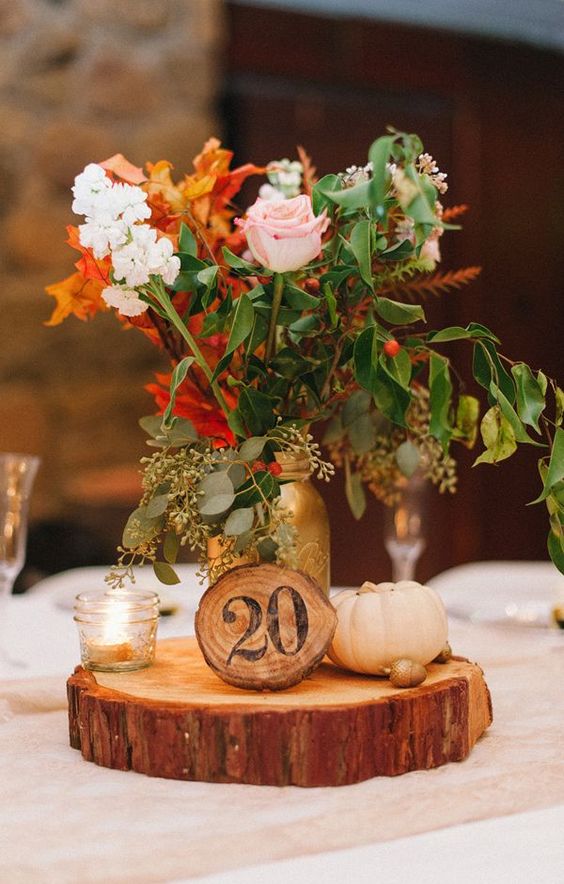 A-fall-wedding-centerpiece-of-a-wood-slice-pumpkins-candles-and-bright-fall-blooms-in-a-gold-jar