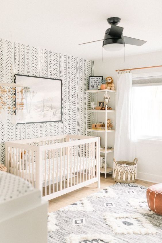 A-neutral-boho-nursery-with-a-printed-wall-a-printed-rug-a-leather-ottoman-a-white-crib-and-a-woven-basket