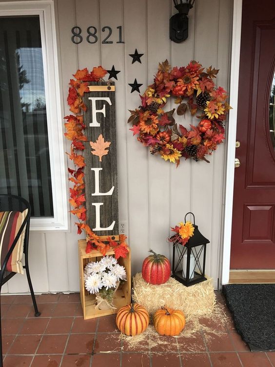 A-reclaimed-wood-fall-sign-topped-with-bright-fake-leaves-faux-pumpkins-a-wreath-hay-and-a-lantern