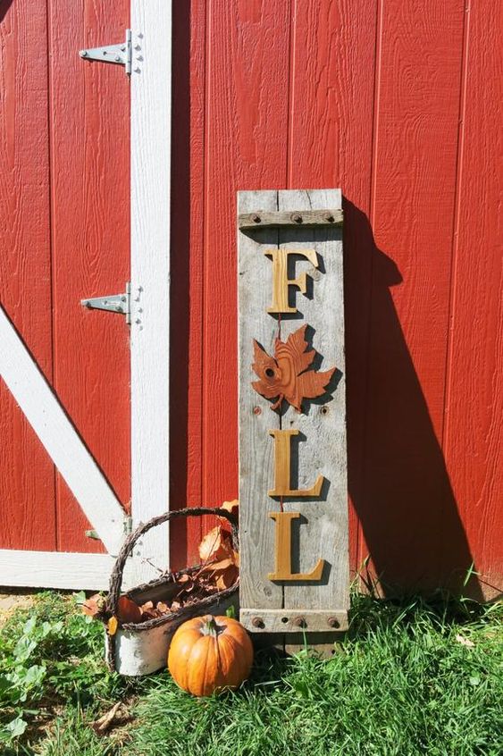 A-reclaimed-wood-fall-sign-with-yellow-letters-and-a-red-leaf-pumpkins-and-a-basket-with-leaves