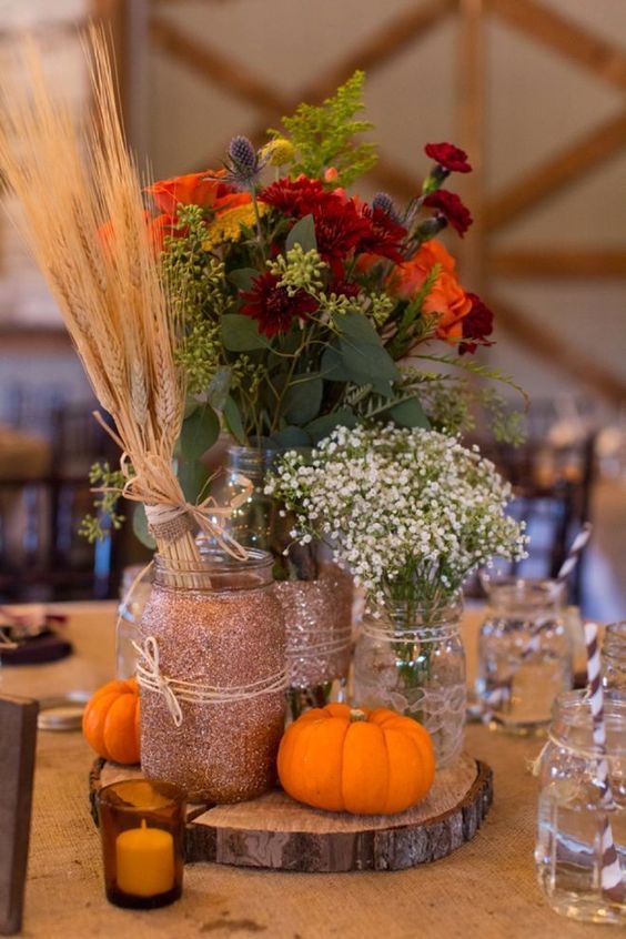 A-rustic-fall-centerpiece-of-a-wood-slice-pumpkins-candles-bright-blooms-babys-breath-and-a-wheat-bundle
