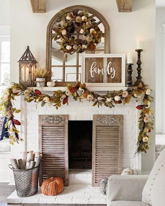 A-rustic-fall-mantel-with-dried-fall-leaves-and-pumpkins-candles-in-wooden-candle-holders-wheat-arrangements-and-a-rustic-sign