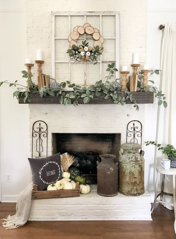 A-rustic-fall-mantel-with-greenery-candles-in-wooden-candleholders-a-crate-with-white-pumpkins-a-pillow-and-a-wood-slice-wreath
