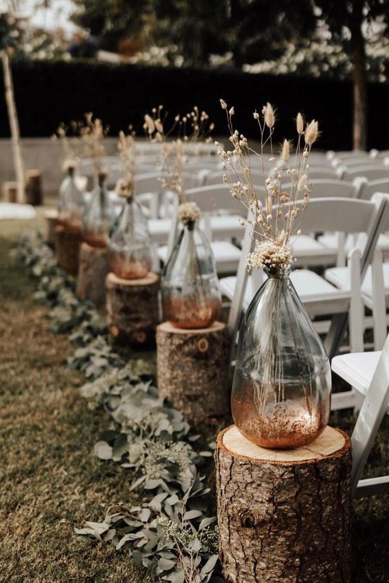 A-rustic-fall-wedding-arch-with-tree-stumps-vases-with-dried-grasses-and-blooms-and-eucalyptus