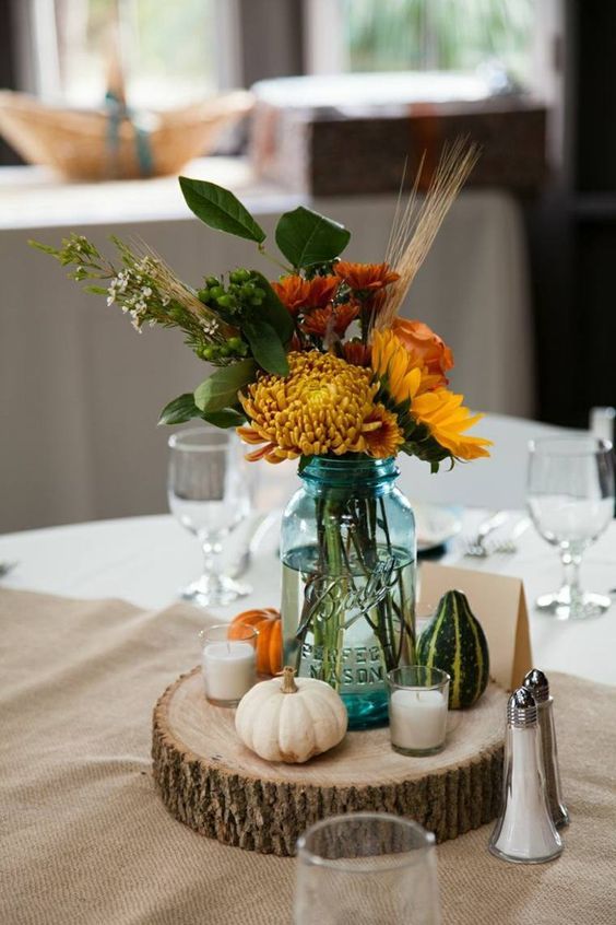 A-rustic-fall-wedding-centerpiece-of-a-wood-slice-candles-pumpkins-and-bright-fall-blooms-and-wheat-in-a-jar