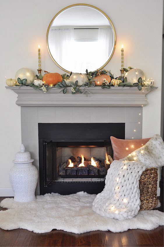 A-simple-contemporary-fall-mantel-done-with-greenery-and-pumpkins-of-muted-colors-plus-lights-all-over-it