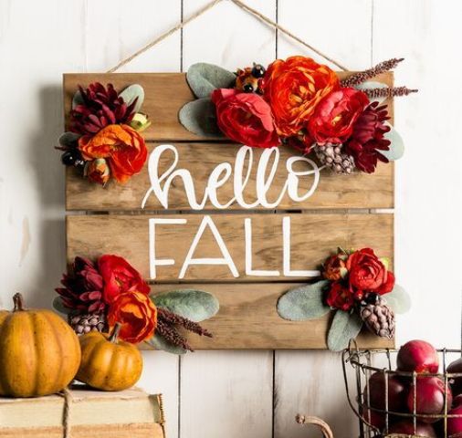 A-stained-wooden-plaque-sign-decorated-with-bright-faux-blooms-greenery-and-even-pinecones