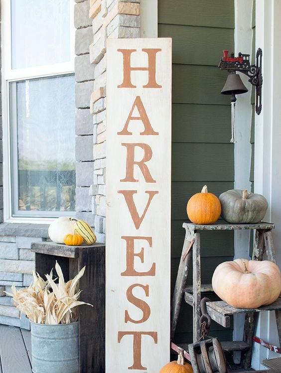 A-tall-harvest-sign-corn-husks-in-a-bucket-and-various-colorful-pumpkins-around-for-a-fall-feel