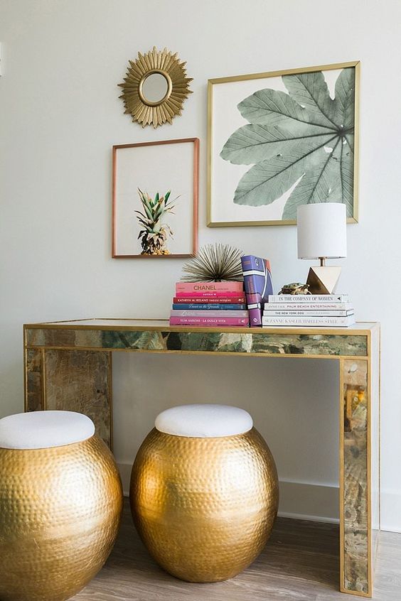 26-an-encrusted-console-table-colorful-books-tropical-artworks-over-the-table-and-hammered-metal-ottomans
