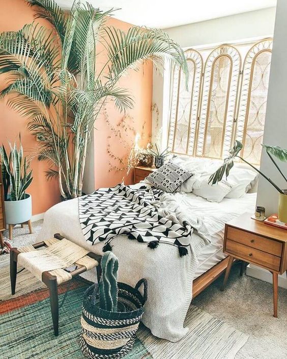 A-bright-boho-bedroom-with-a-rattan-screen-wooden-furniture-a-peachy-wall-potted-plants-and-greenery-and-a-wicker-stool