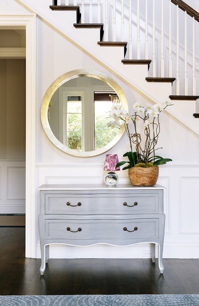 Clean-and-elegant-decor-with-sparkling-round-mirror-and-dresser-near-stairway
