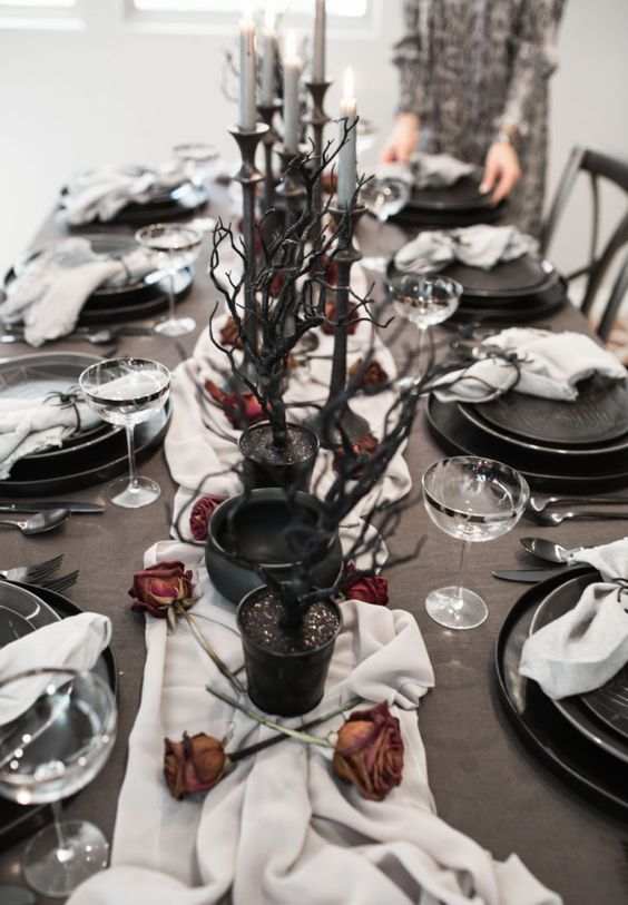 A-halloween-tablescape-with-a-white-runner-dried-roses-black-branches-grye-candles-and-elegant-black-plates
