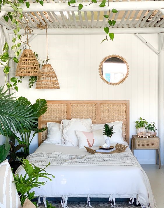 A-boho-tropical-bedroom-done-in-neutrals-a-white-wooden-ceiling-woven-pendant-lamps-and-a-cool-rattan-headboard-plus-lots-of-greenery