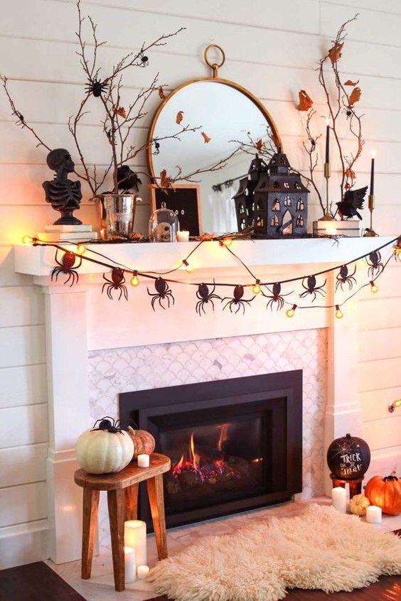 A-catchy-halloween-mantel-with-a-spider-garland-lights-branches-with-leaves-a-scary-house-and-some-pumpkins-on-the-floor