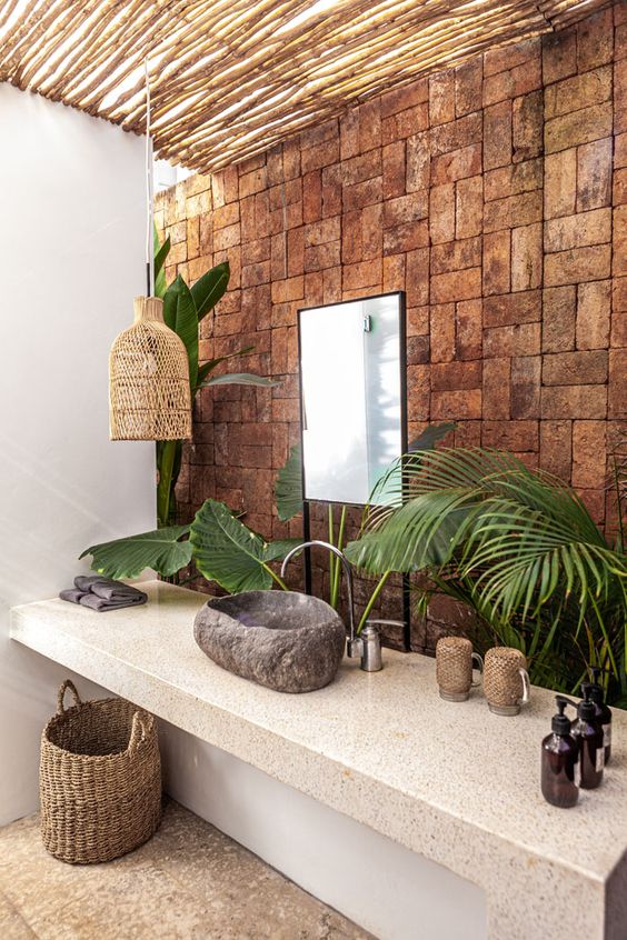 A-catchy-tropical-bathroom-with-a-brick-wall-a-stone-vanity-a-stone-sink-a-woven-lamp-and-a-basket