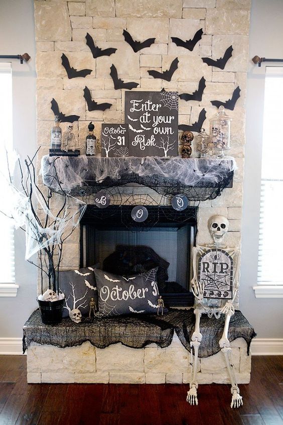 A-chic-halloween-mantel-with-paper-bats-spiderweb-apothecary-bottles-skulls-and-black-pillows-and-a-skeleton