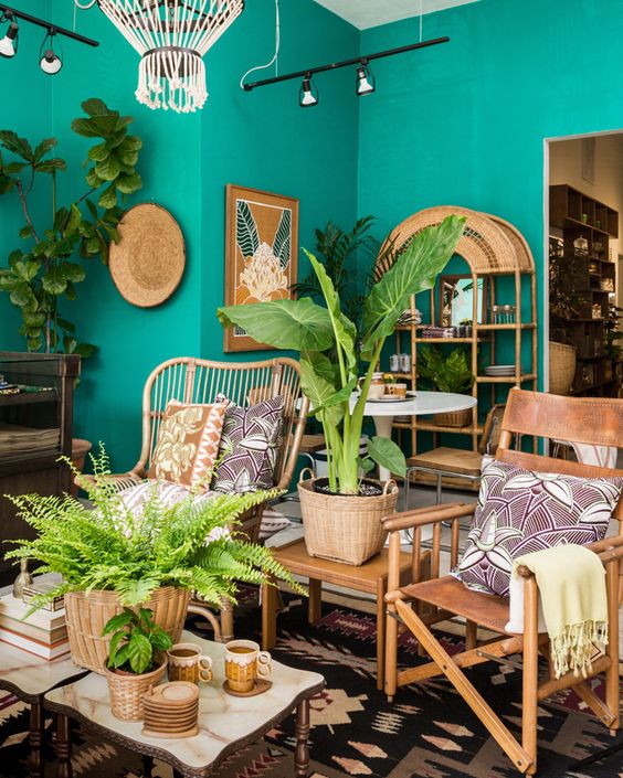 A-colorful-tropical-living-room-with-emerald-walls-rattan-and-leather-furniture-a-gold-mirror-potted-plants-and-bold-artworks