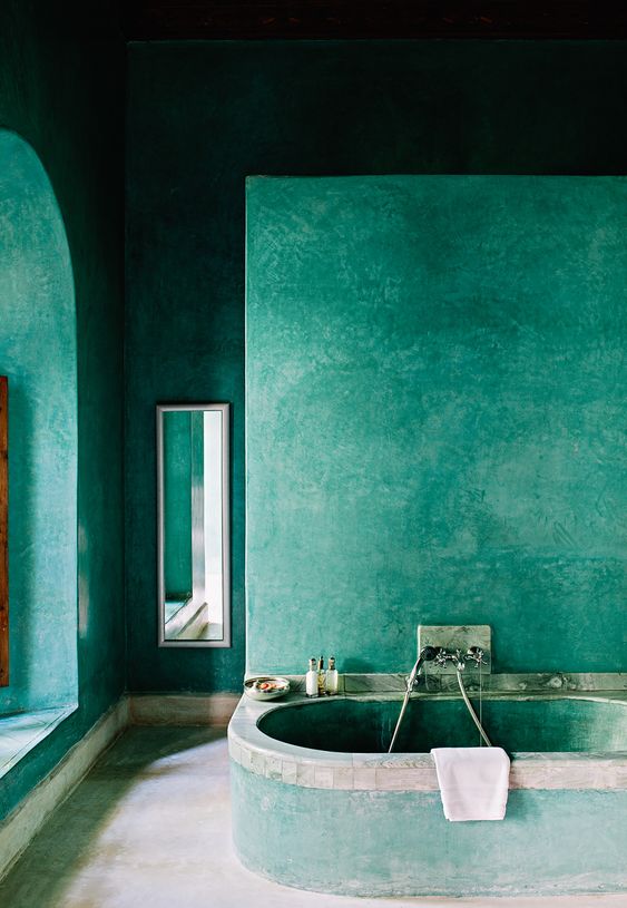 A-green-moroccan-style-bathroom-with-everything-of-concrete-and-plaster-with-a-small-mirror-and-built-in-tub