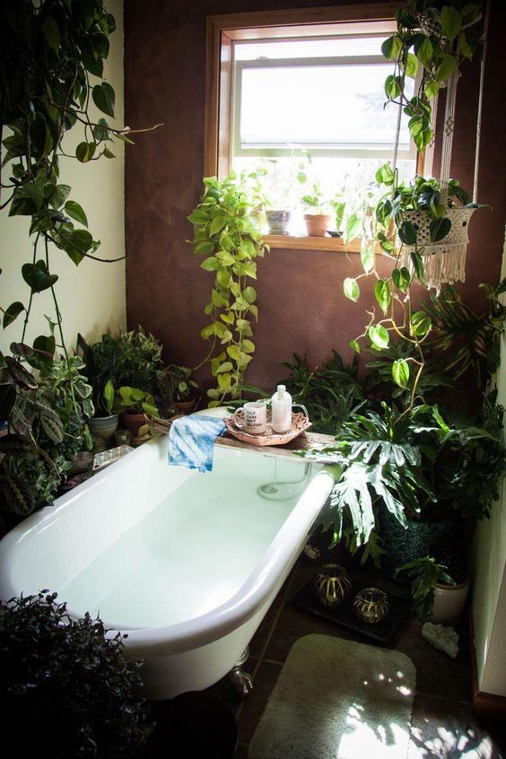 A-home-space-in-boho-style-with-lots-of-potted-greenery-and-climbing-plants-a-bathtub-and-candles-is-cool