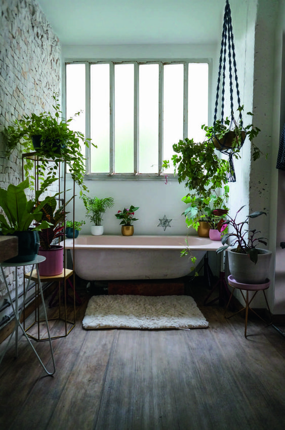 A-pretty-moody-bathroom-with-a-pink-tub-colorful-planters-with-greenery-all-around-and-a-brick-wall-for-interest