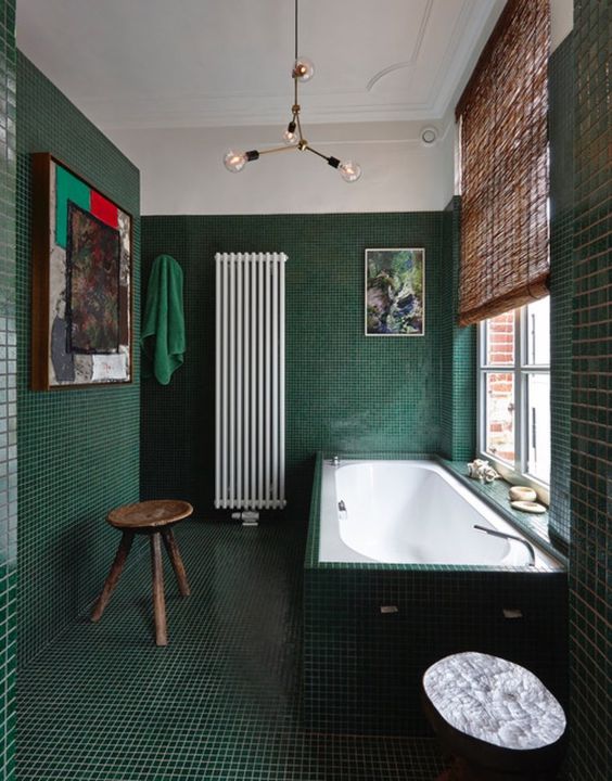 A-refined-dark-green-bathroom-all-clad-with-tiles-including-the-tub-a-modern-chandelier-a-wooden-stool-and-some-pretty-artworks