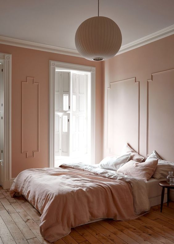 A-refined-vintage-inspired-bedorom-with-blush-molding-walls-blush-and-white-bedding-a-wooden-floor-and-a-paper-lamp