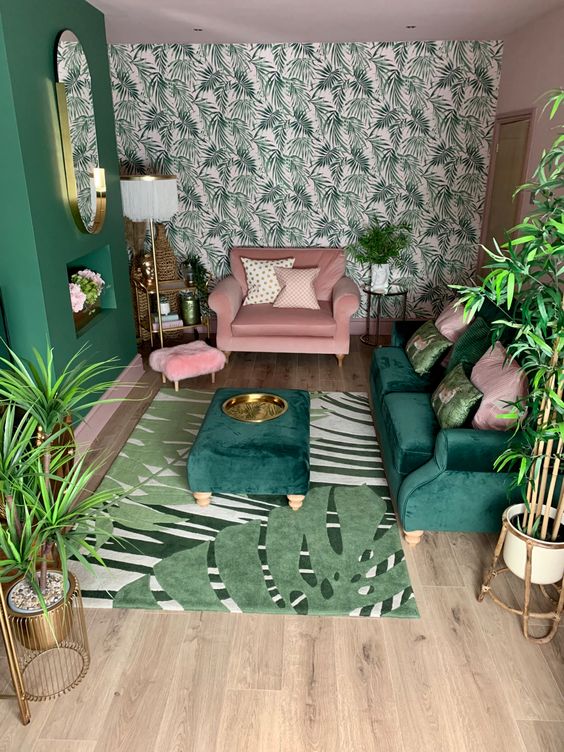 A-small-tropical-living-room-with-a-tropical-leaf-wall-a-green-sofa-and-ottoman-a-pink-chair-touches-of-gold