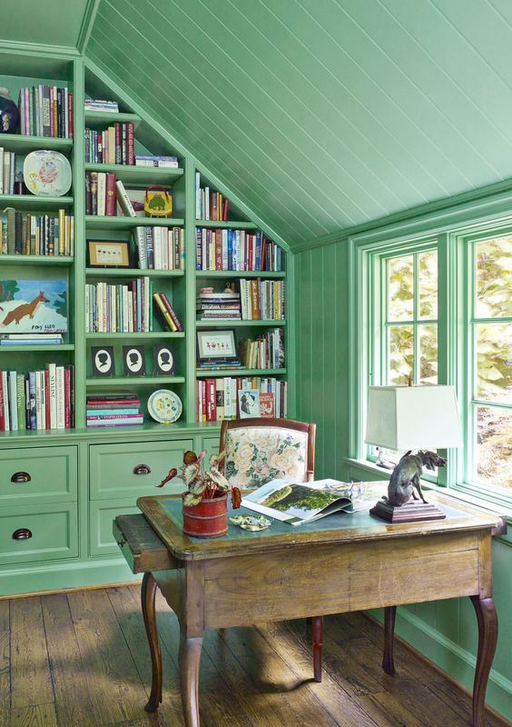 A-vintage-inspired-home-office-in-sage-green-with-a-rough-wooden-desk-a-large-wall-storage-unit-taking-the-whole-wall