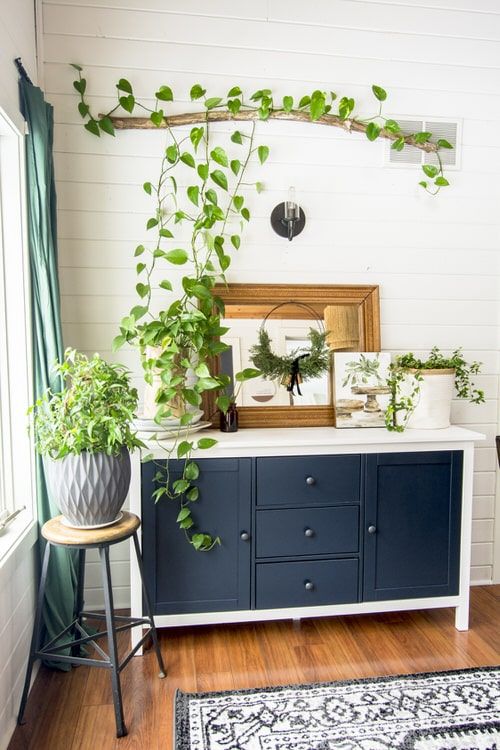 A-vintage-sideboard-with-some-potted-greenery-a-stick-and-greenery-installation-over-it-and-a-grey-planter-with-greenery